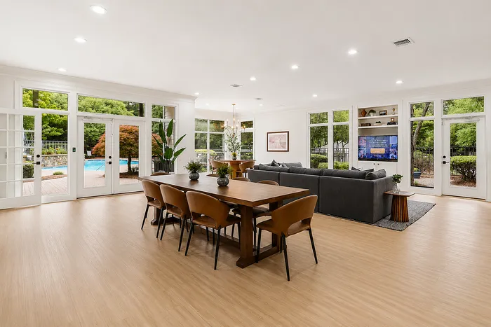 Bright open-concept living space with elegant dining area, cozy seating, and full-height windows overlooking a luxurious pool.