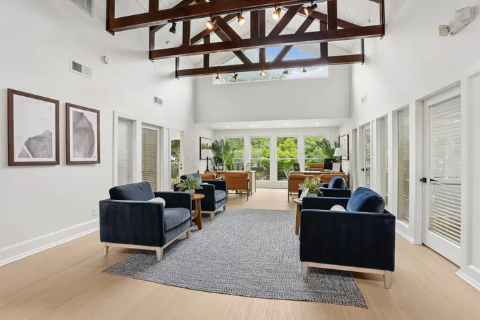 Inviting living space with high ceilings and wooden beams, featuring elegant navy seating, contemporary decor, and large windows offering garden views.
