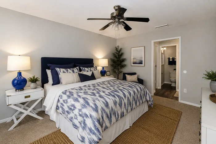 Elegant bedroom with a plush bed, stylish blue and white decor, and cozy lighting, leading to an en-suite bathroom.