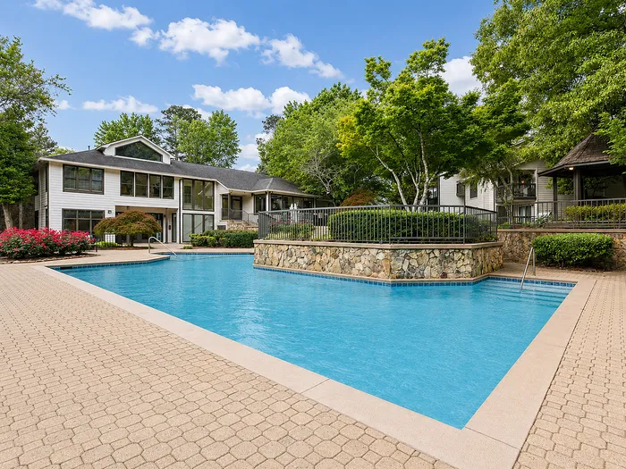 Luxurious apartment complex featuring a pristine swimming pool, lush landscaped gardens, and elegant architecture under a clear blue sky.