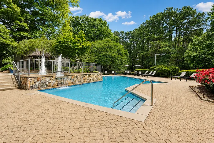 Luxurious outdoor pool area surrounded by lush greenery, featuring elegant lounge chairs and a charming gazebo.