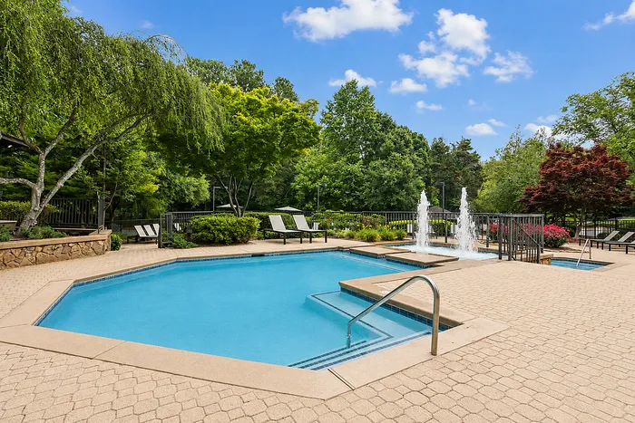 Beautiful outdoor pool area surrounded by lush greenery and comfortable lounge chairs, featuring a serene water fountain.