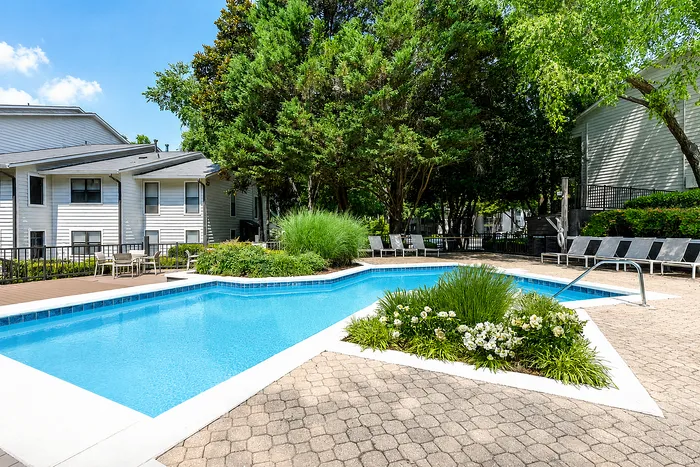 Inviting outdoor pool area surrounded by lush greenery and comfortable lounge chairs, perfect for relaxation in a serene apartment community.