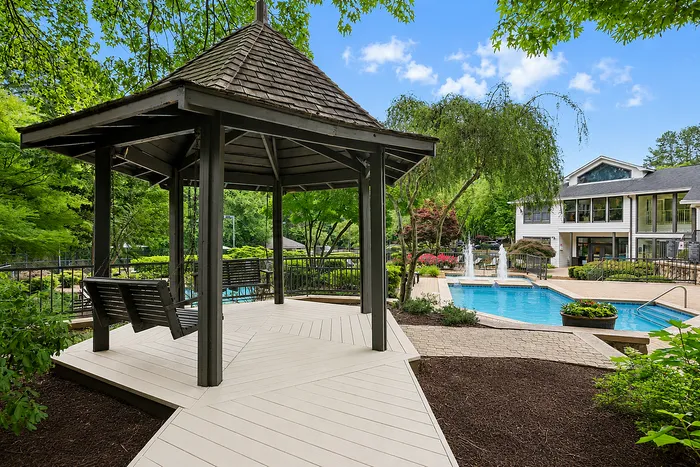 Charming outdoor gazebo with swinging benches overlooking a sparkling pool and lush landscaping.