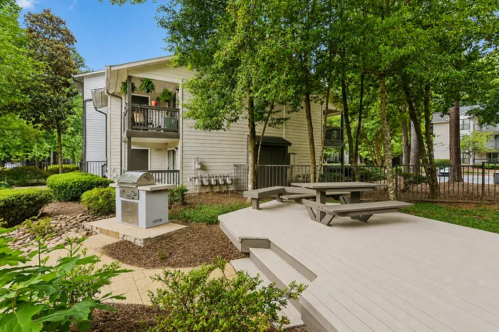 Charming apartment exterior with lush greenery, a cozy balcony, and a welcoming outdoor picnic area featuring a barbecue grill.
