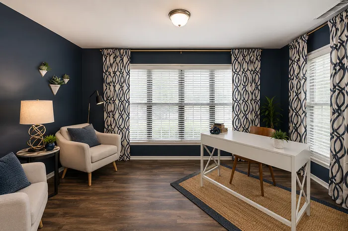 Elegant home office with stylish navy walls, cozy armchairs, and a sleek white desk, showcasing modern decor and abundant natural light.