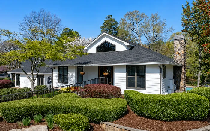 Charming white house surrounded by lush greenery, featuring a stylish stone chimney and inviting windows under a clear blue sky.