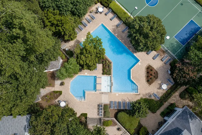 Aerial view of luxurious pool area with surrounding lounge chairs, lush greenery, and adjacent sports courts, offering a perfect retreat for relaxation and recreation.