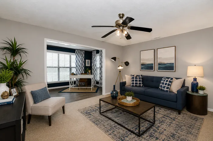 Chic living room with modern navy decor, featuring a comfy blue sofa, stylish coffee table, and an inviting home office space with large windows.