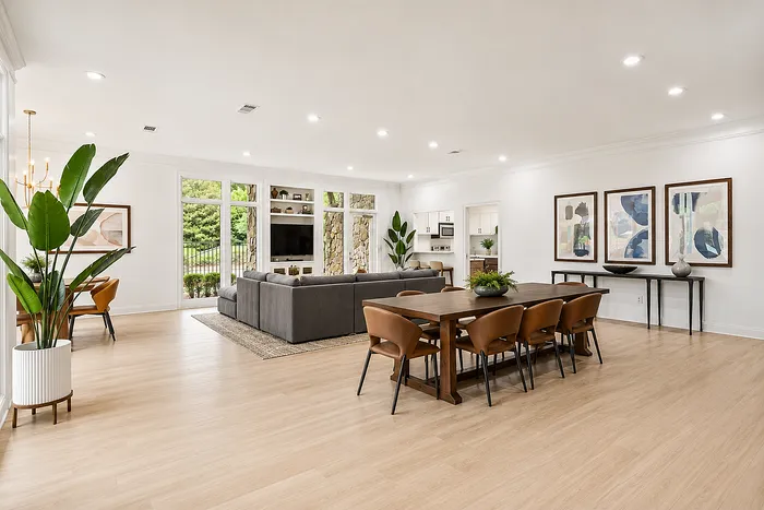 Elegant open-concept living and dining area with sleek hardwood flooring, chic decor, and large windows offering lush garden views.