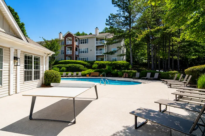 Inviting outdoor pool area with stylish loungers and lush greenery, perfect for relaxation. Modern apartment building in the background enhances the serene setting.