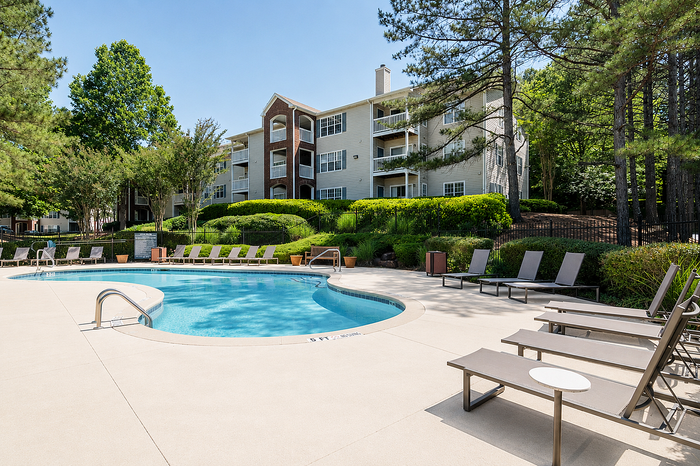 Inviting outdoor pool surrounded by lush greenery and elegant apartment building, perfect for relaxation and leisure.