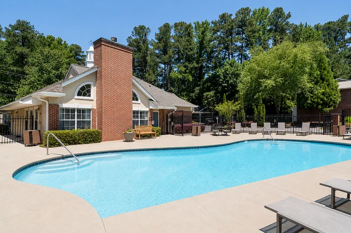 Inviting apartment complex with a pristine outdoor pool, surrounded by lush greenery and stylish brick architecture, perfect for relaxation and leisure.