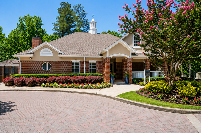 Charming brick apartment building with beautifully landscaped gardens, surrounded by vibrant flowers and lush greenery, offering an inviting and tranquil setting.