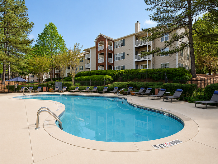 Charming apartment complex featuring a serene outdoor pool surrounded by lush greenery, ideal for relaxation and leisure.