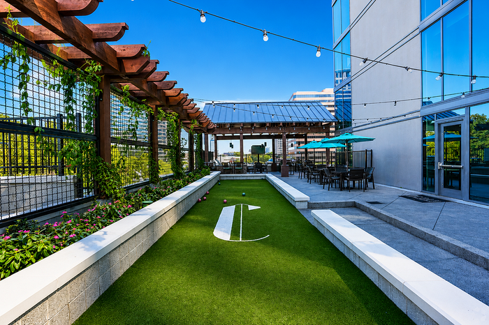 Modern rooftop patio featuring lush greenery, a bocce court, and stylish outdoor seating with colorful umbrellas.