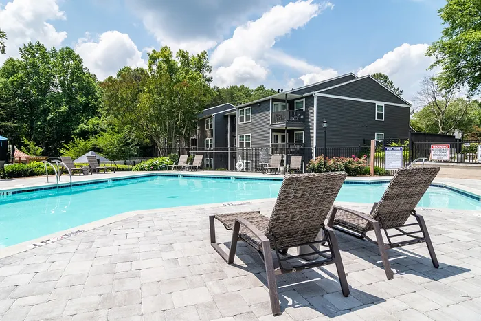 Inviting outdoor pool area with comfortable lounge chairs and a modern apartment building backdrop, surrounded by lush greenery for a serene living experience.