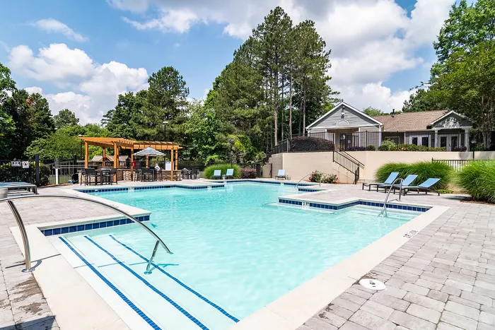 Inviting outdoor pool area with sun loungers, surrounded by lush greenery and a charming pergola, perfect for relaxation.