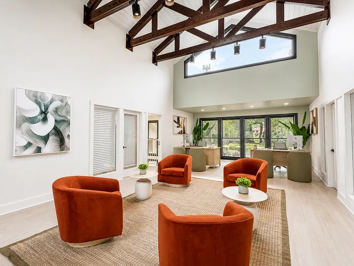 Bright and airy lounge with stylish orange chairs, high ceilings, and natural light through large windows offering a view of greenery.