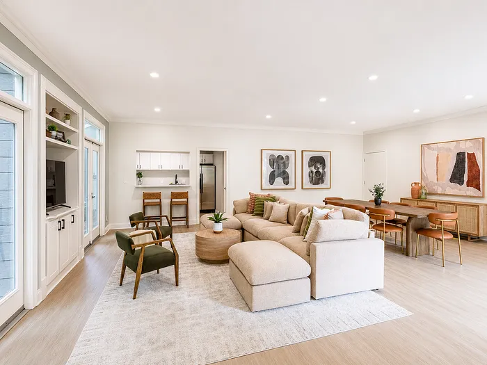 Elegant open-concept living room featuring a cozy beige sectional, modern dining area, and sleek kitchen with abundant natural light.