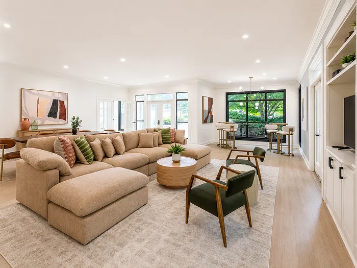 Spacious living area with elegant beige sectional, stylish bar stools, and floor-to-ceiling windows showcasing natural light.