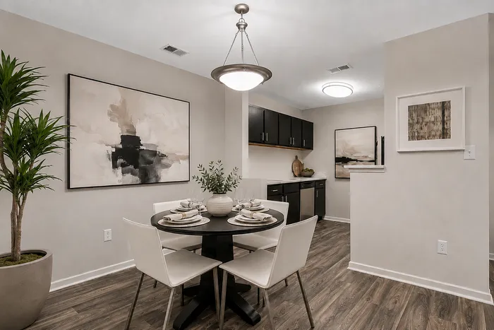 Elegant dining area with a modern round table set for four, complemented by chic artwork and warm-toned flooring, adjacent to a stylish kitchen with sleek cabinetry.