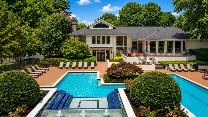 Luxurious building exterior with a sparkling blue pool, surrounded by lush greenery and elegant lounge chairs, perfect for relaxation.
