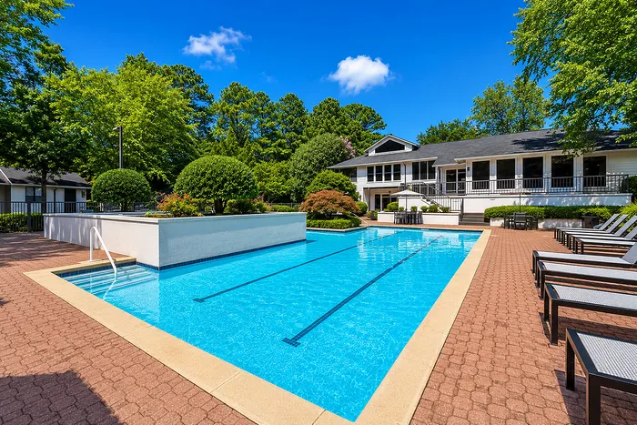 Luxurious apartment complex showcasing a sparkling swimming pool surrounded by lush greenery and elegant lounge chairs, perfect for relaxation.