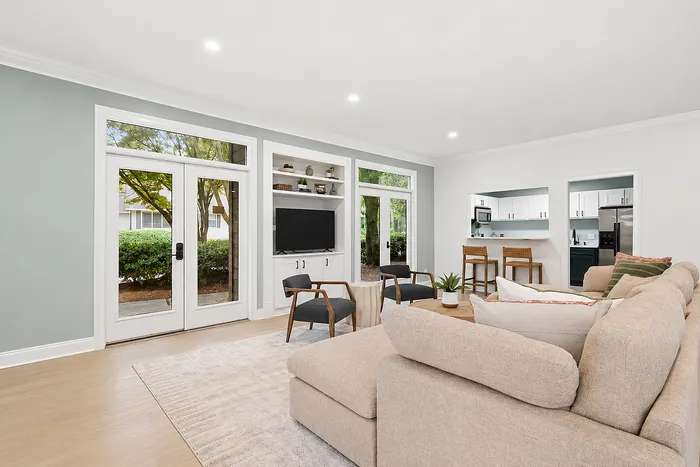 Bright and inviting living room featuring large windows, a cozy sectional sofa, and an open-concept kitchen with modern appliances.