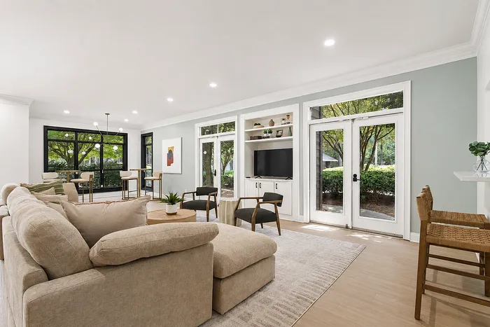 Elegant open-concept living area with plush sofas, stylish bar stools, and large windows offering lush garden views.