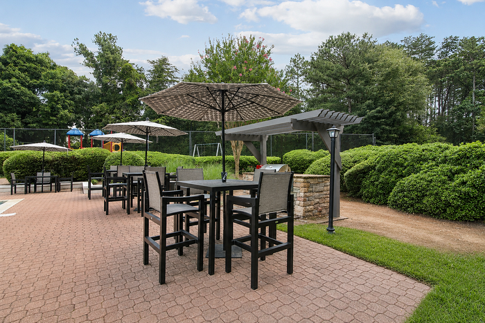 Inviting outdoor patio area with stylish seating, shaded by elegant umbrellas, surrounded by lush greenery for a relaxing ambiance.