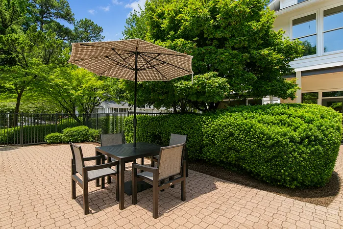 Charming outdoor patio with elegant dining set and a stylish umbrella, surrounded by lush greenery for a serene ambiance.
