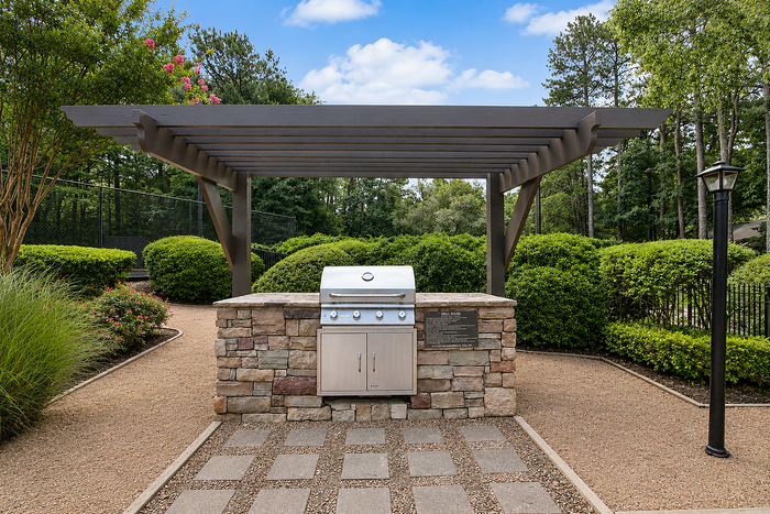 Charming outdoor grilling area with a stone barbecue setup beneath an elegant pergola, surrounded by lush greenery.
