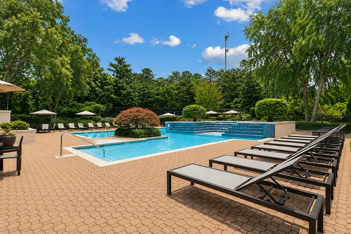 Inviting outdoor pool area with elegant loungers, lush greenery, and a clear blue sky, perfect for relaxation and leisure.