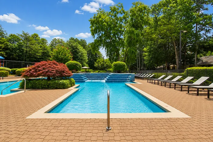 Inviting outdoor swimming pool with cascading waterfalls, surrounded by lush greenery and comfortable lounge chairs, perfect for relaxing under a bright blue sky.