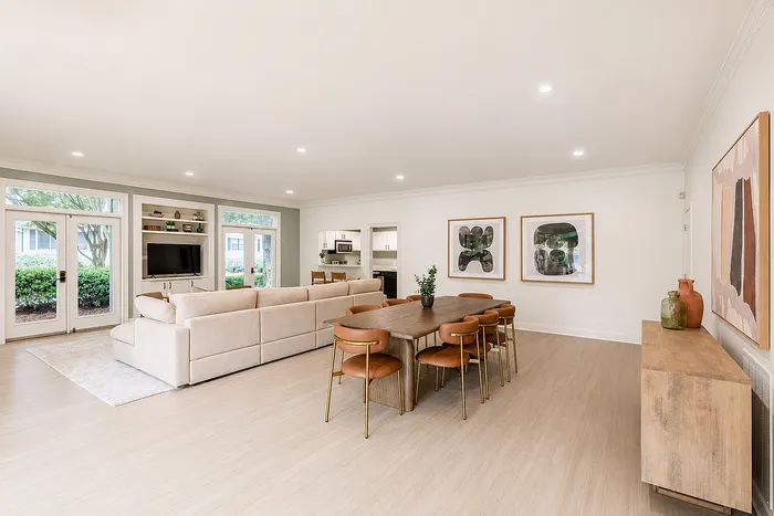 Elegant open-concept living and dining area with natural light, featuring a modern sectional sofa, stylish dining set, and serene garden views.