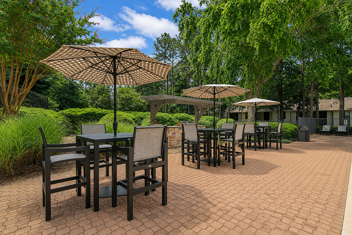 Charming outdoor patio featuring elegant seating with umbrellas, surrounded by lush greenery and vibrant landscaping.