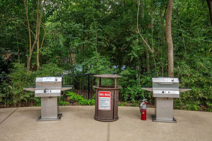 Spacious outdoor grilling area with two shiny silver barbecue grills, surrounded by lush greenery.