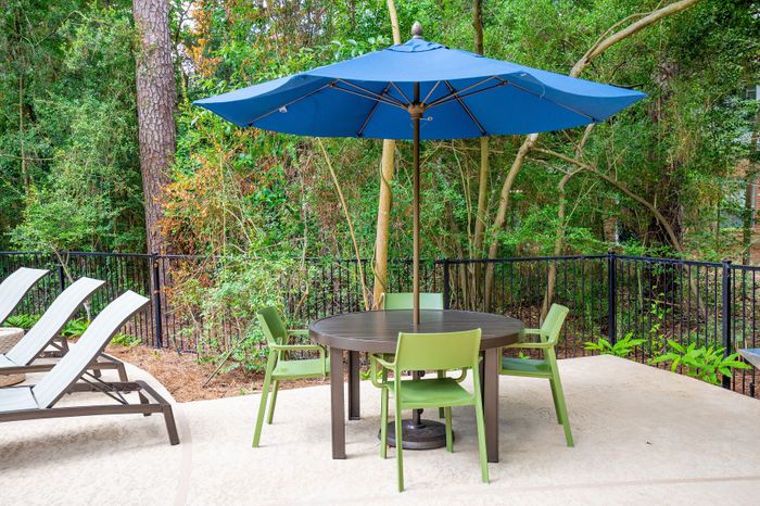 Charming outdoor patio with a round table, vibrant green chairs, and a large blue umbrella.