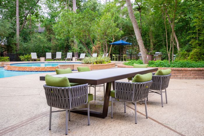 Charming outdoor space with elegant poolside seating, green-cushioned chairs, and a welcoming dining table surrounded by lush greenery.