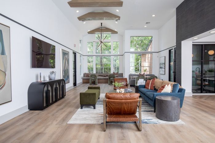 Modern area featuring high ceilings, floor-to-ceiling windows, stylish wood flooring, elegant art, and cozy seating options.