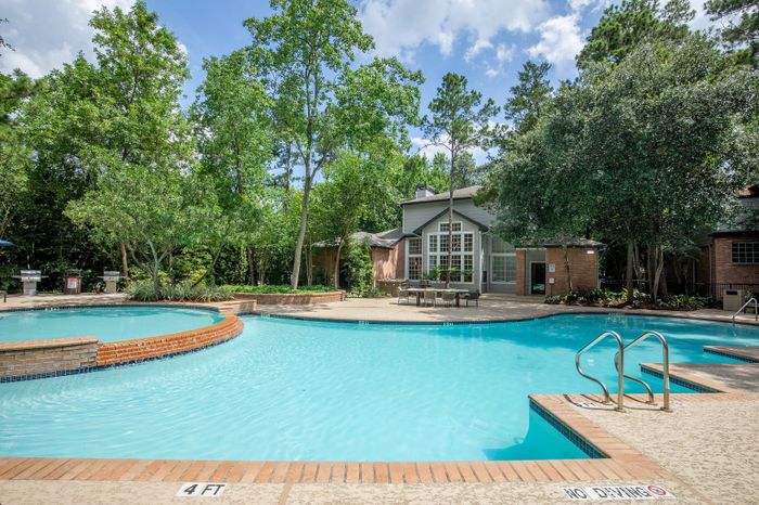 Inviting swimming pool surrounded by lush greenery and stylish patio in a serene apartment community.