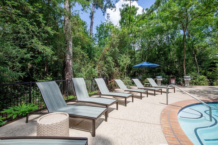Inviting outdoor pool area surrounded by lush greenery, featuring comfortable lounge chairs and barbecue grills for a relaxing retreat.