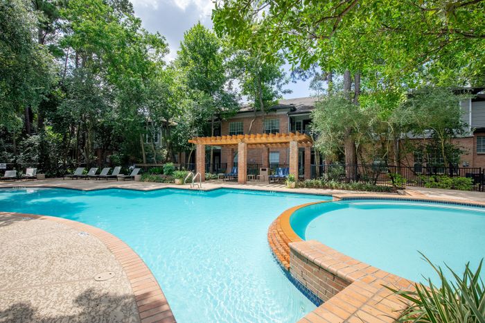 Luxurious apartment complex with an inviting swimming pool, relaxing loungers, and lush greenery surrounding a tasteful pergola area.