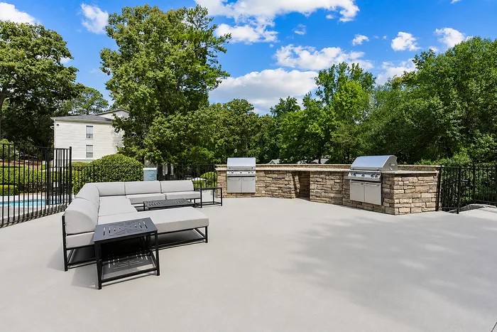 Inviting outdoor patio with modern stone BBQ grills and lush greenery at Avana Cumberland luxury apartment community.