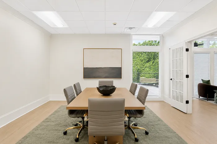Elegant conference room with modern leather chairs around a wooden table, featuring large windows offering natural light and a serene view.