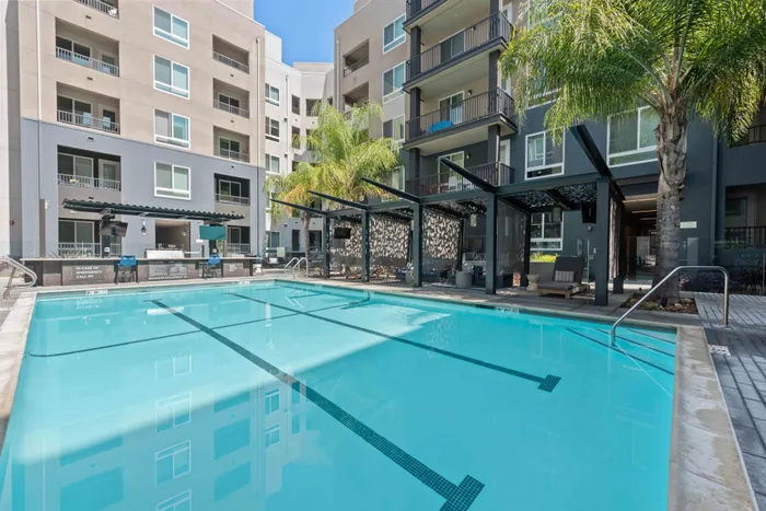 Luxurious apartment complex featuring a sparkling swimming pool, modern pergolas, and lush palm trees for a resort-style living.