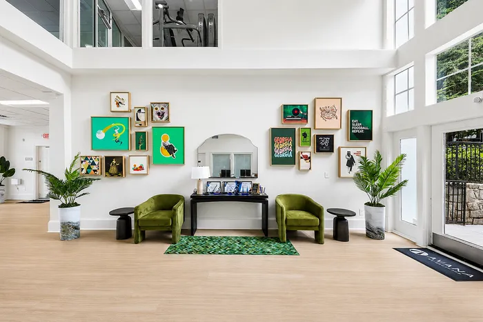 Inviting apartment lobby with modern art gallery wall, elegant green chairs, and ample natural light.