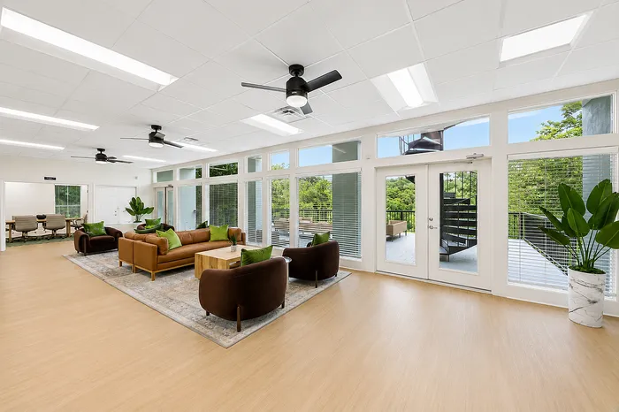 Bright, spacious living room with modern furniture, large windows, and access to a private balcony overlooking lush greenery.