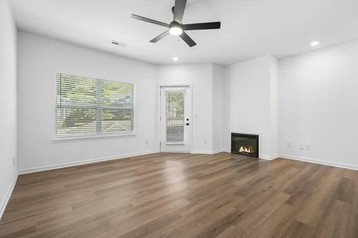 Bright, spacious living room with modern wood flooring, sleek ceiling fan, and a cozy corner fireplace, complemented by ample natural light from large windows.